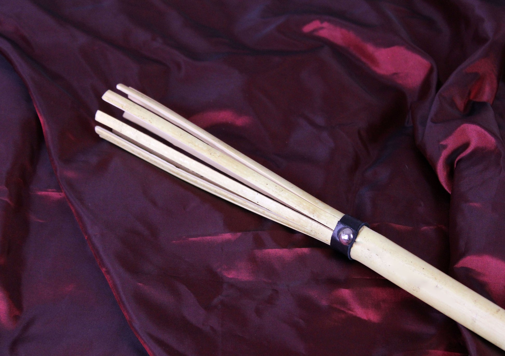 Détail de la canne bdsm en bambou, fendu en plusieurs tiges, associées par une lanière de cuir