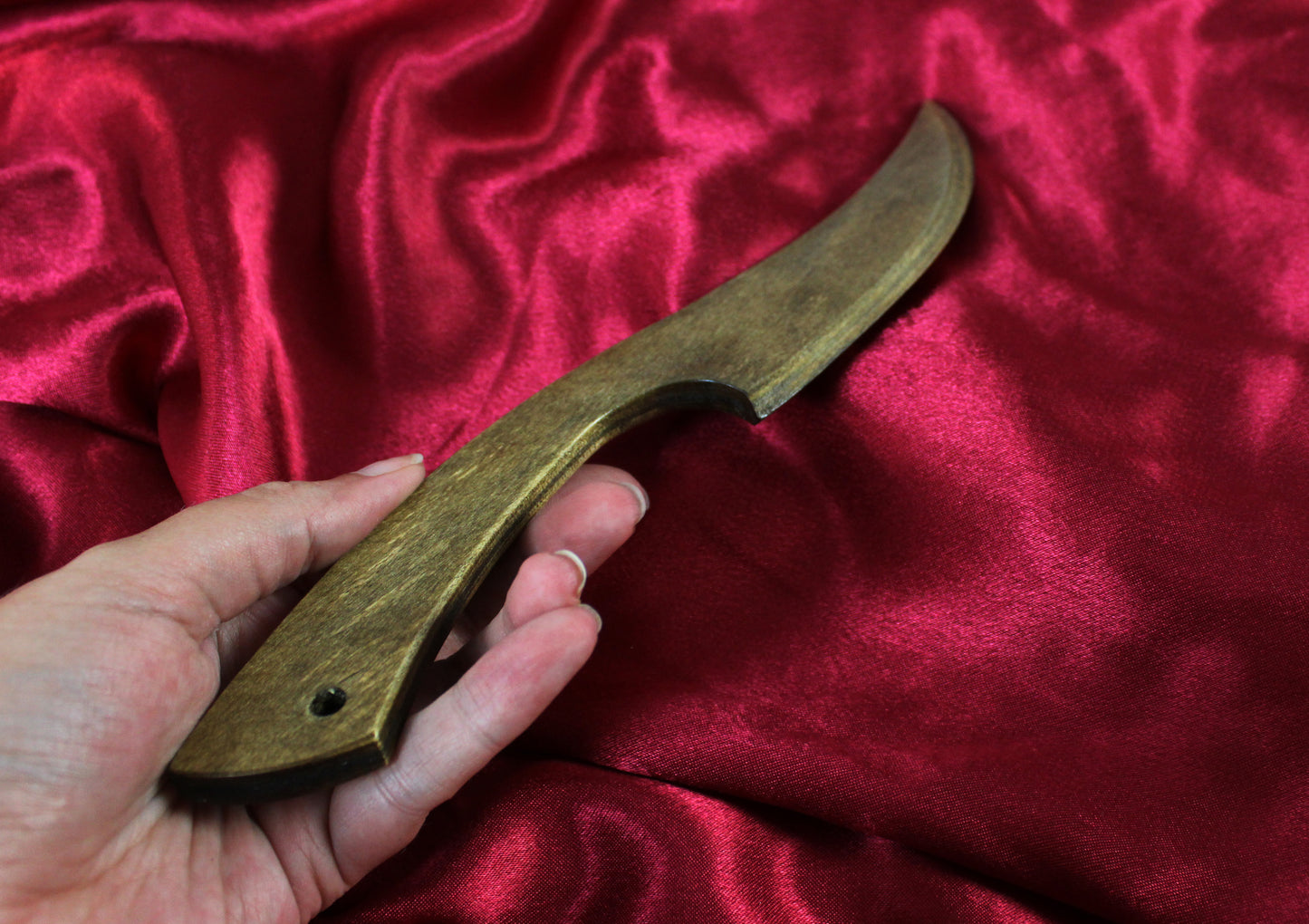 couteau bdsm en bois, vue légèrement de côté, tenu en main