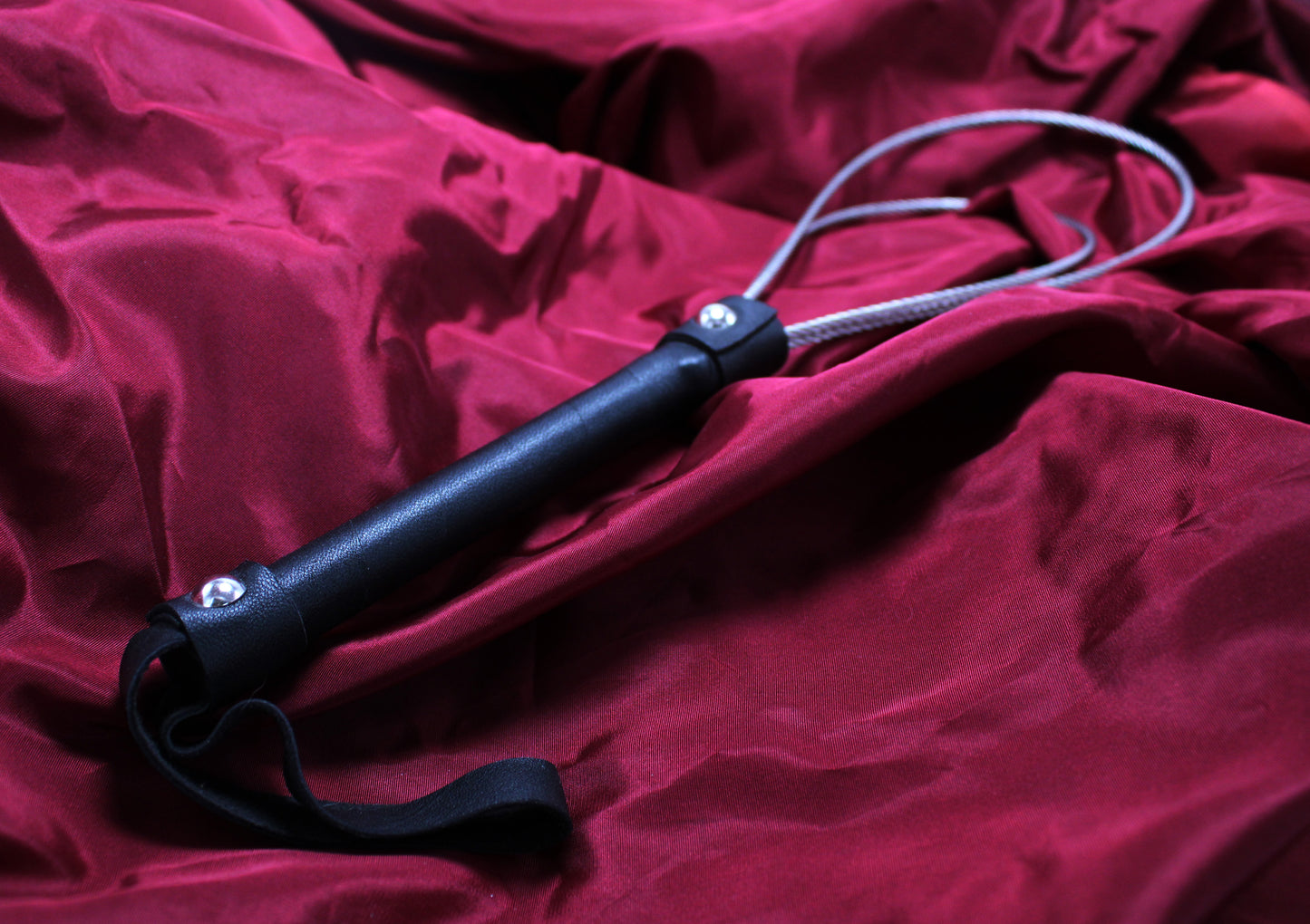 paddle en câble en acier, vue du manche en cuir avec dragonne, sur fond de satin bordeaux