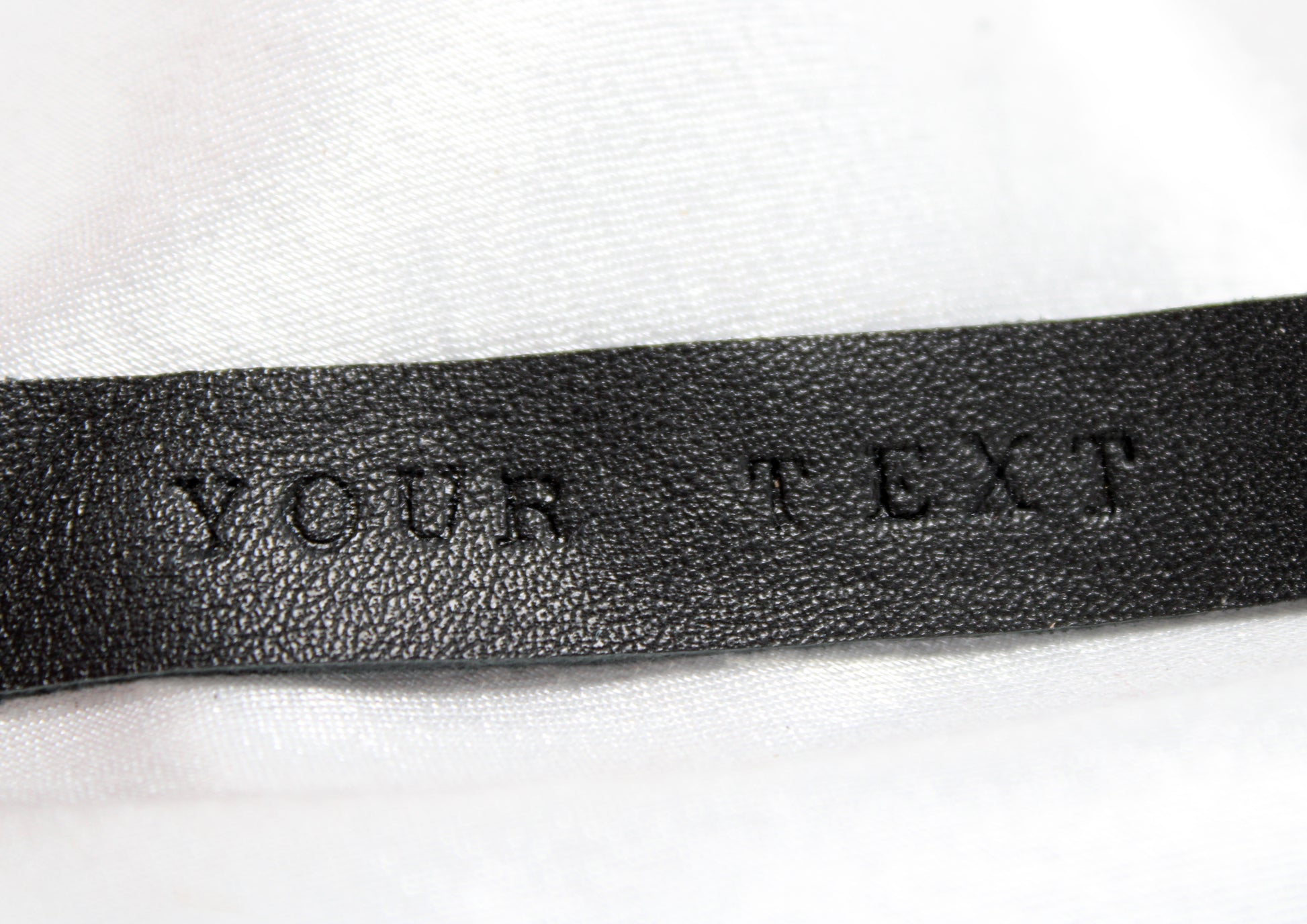 Inscription de personnalisation sur la dragonne en cuir, est écrit "YOUR TEXT" avec des lettres martelées, en impression dans le cuir.
